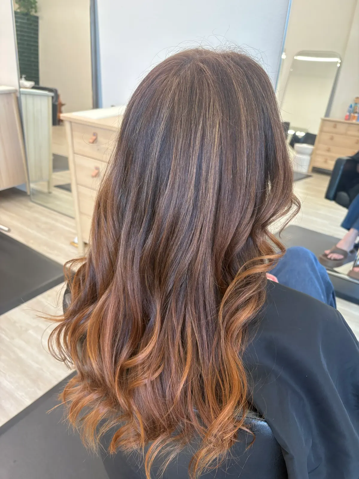 Long brunette hair with warm caramel balayage highlights styled in soft loose waves.
