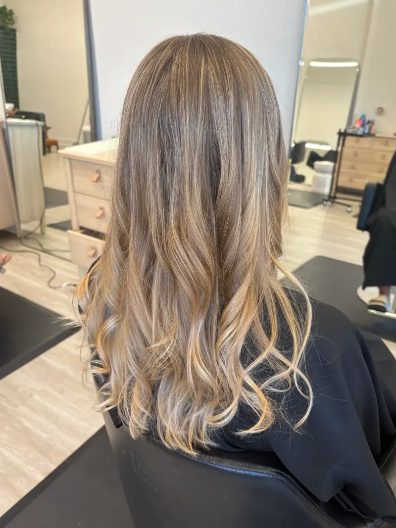 Long blonde hair with beige and golden highlights, a soft darker root, and loose curls.