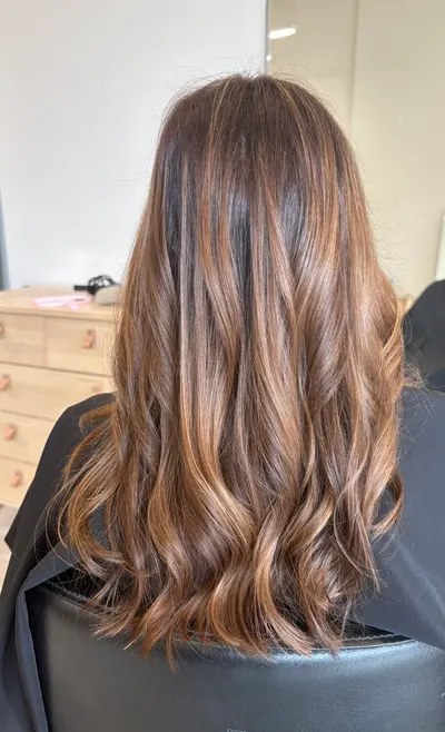 Back view of long brunette hair with bold caramel highlights from a darker root, curled into loose waves.