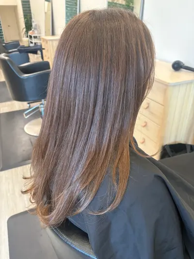 Side view of long, straight brunette hair with subtle caramel highlights and curved, layered ends.