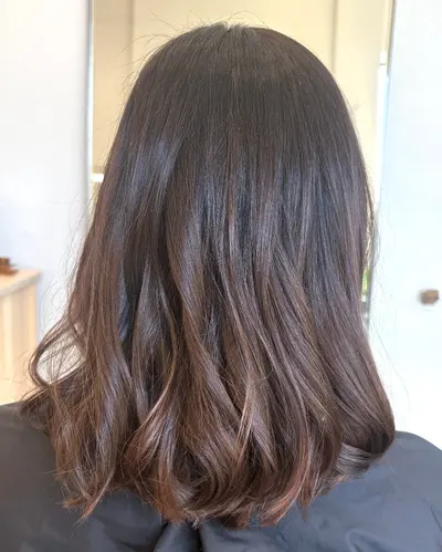 Back view of shoulder-length dark brunette hair with soft, light brown balayage through the wavy ends.