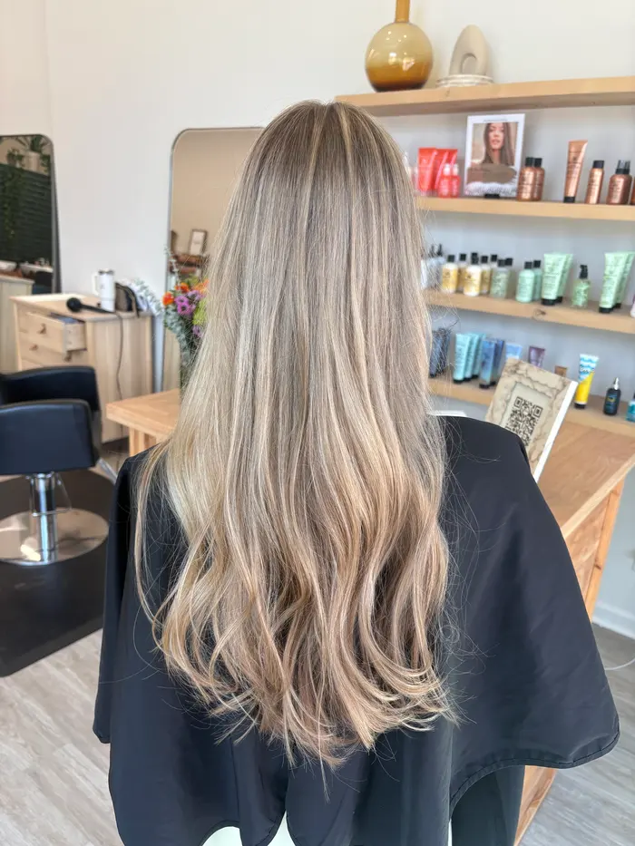 Back view of long, layered beige-blonde balayage with soft waves and a natural, deeper root.