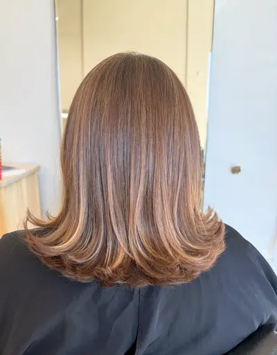 Back view of shoulder-length brunette hair with caramel balayage, soft layers, and ends flipped out.