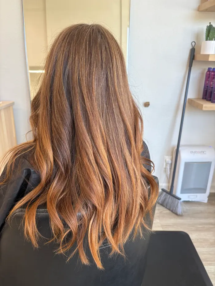 Back view of long brunette hair with copper and caramel balayage that gets brighter toward the wavy ends.